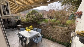 Un patio al aire libre con una mesa, sillas, un muro de piedra y un área cubierta con una pérgola.