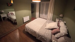 Un dormitorio con una cama, dos mesitas de noche, un radiador, una ventana con cortinas y una lámpara colgante.
