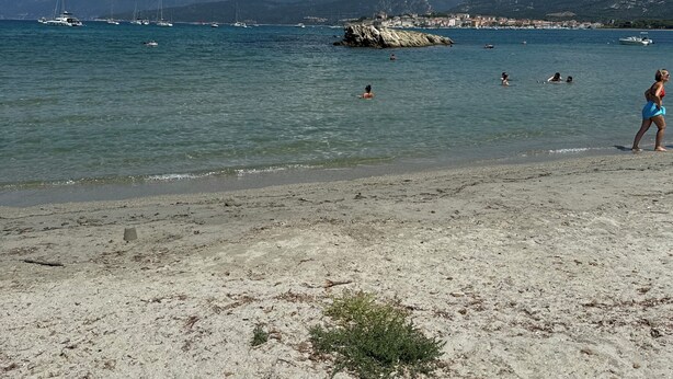 Una playa con agua cristalina, embarcaciones y montañas al fondo.