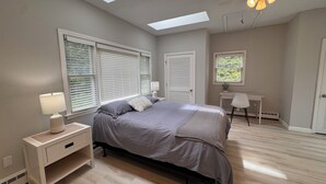 Un dormitorio con cama, escritorio, silla, ventilador de techo y tragaluces.