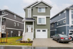 A two-story residential building with a front porch, a garage, and a car parked in the driveway. - Lovely Home in Victoria, BC (Langford)