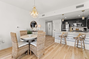 A modern kitchen with a central island, stainless steel appliances, and a dining area with wicker chairs and a chandelier. - Elegant Baytowne Wharf Luxury Getaway (Miramar Beach)