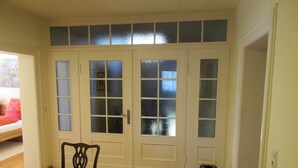 A room with a bed, a chair, a table, and a door with frosted glass panels.