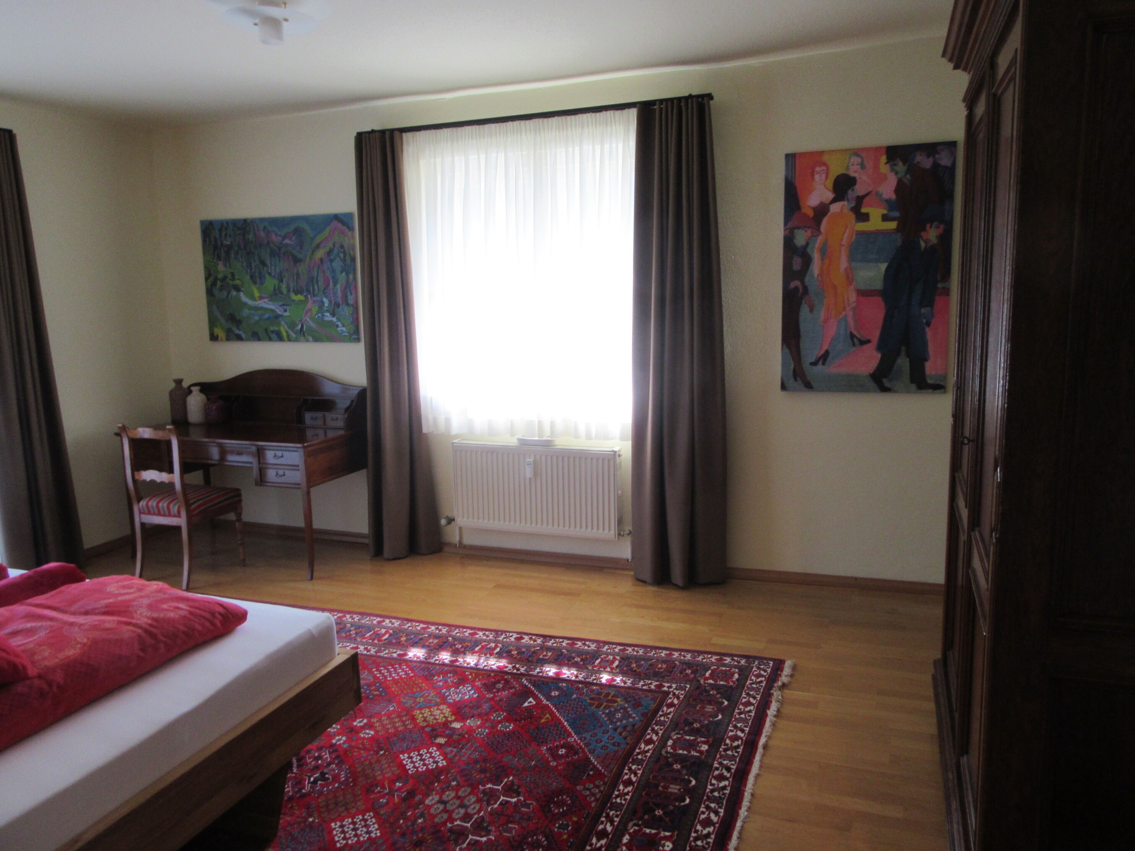 Un dormitorio con una cama, un escritorio, una silla, un radiador y un cuadro en la pared.