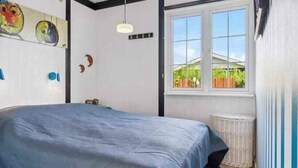 Quarto com cama, janela, parede com obras de arte e luminária no teto.