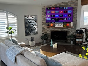 Ein Wohnzimmer mit Kamin, einem flachbildfernseher darüber, einer Couch, einem Couchtisch und einer Topfpflanze.