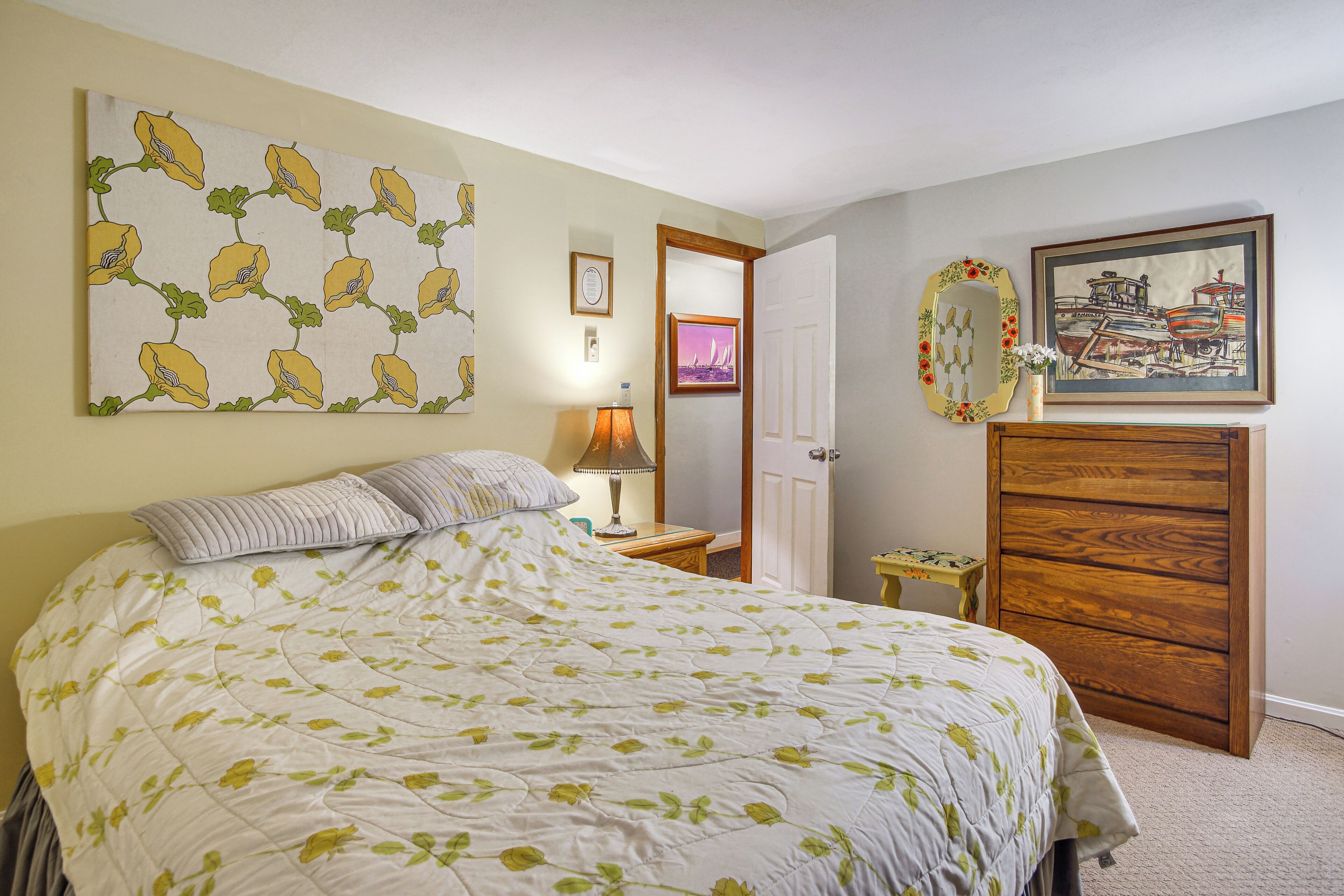 Une chambre à coucher comprenant un lit, une table de chevet, une commode, un miroir et des œuvres d’art murales.