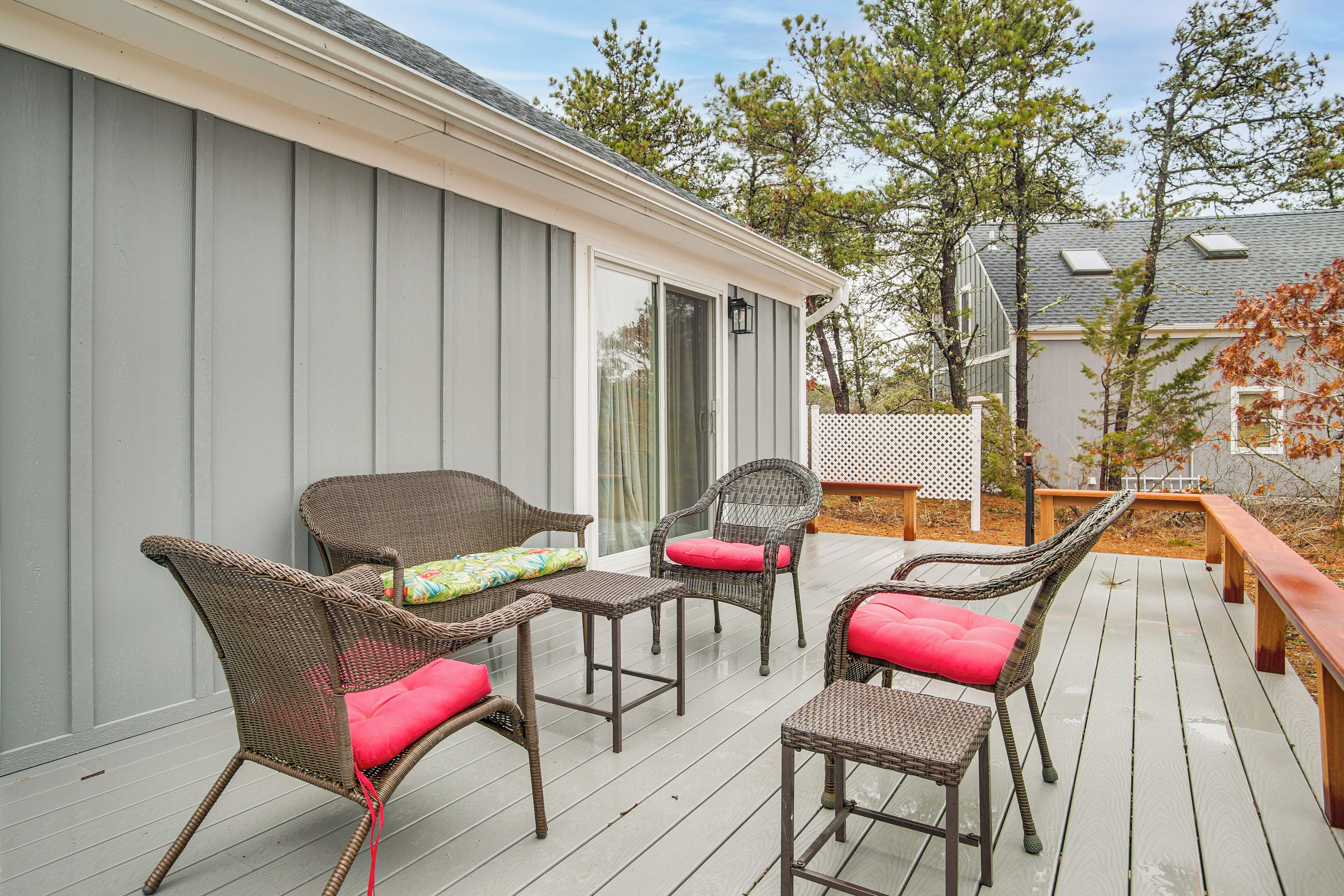 Une terrasse extérieure couverte, aménagée avec des meubles en osier et entourée d’une clôture blanche.