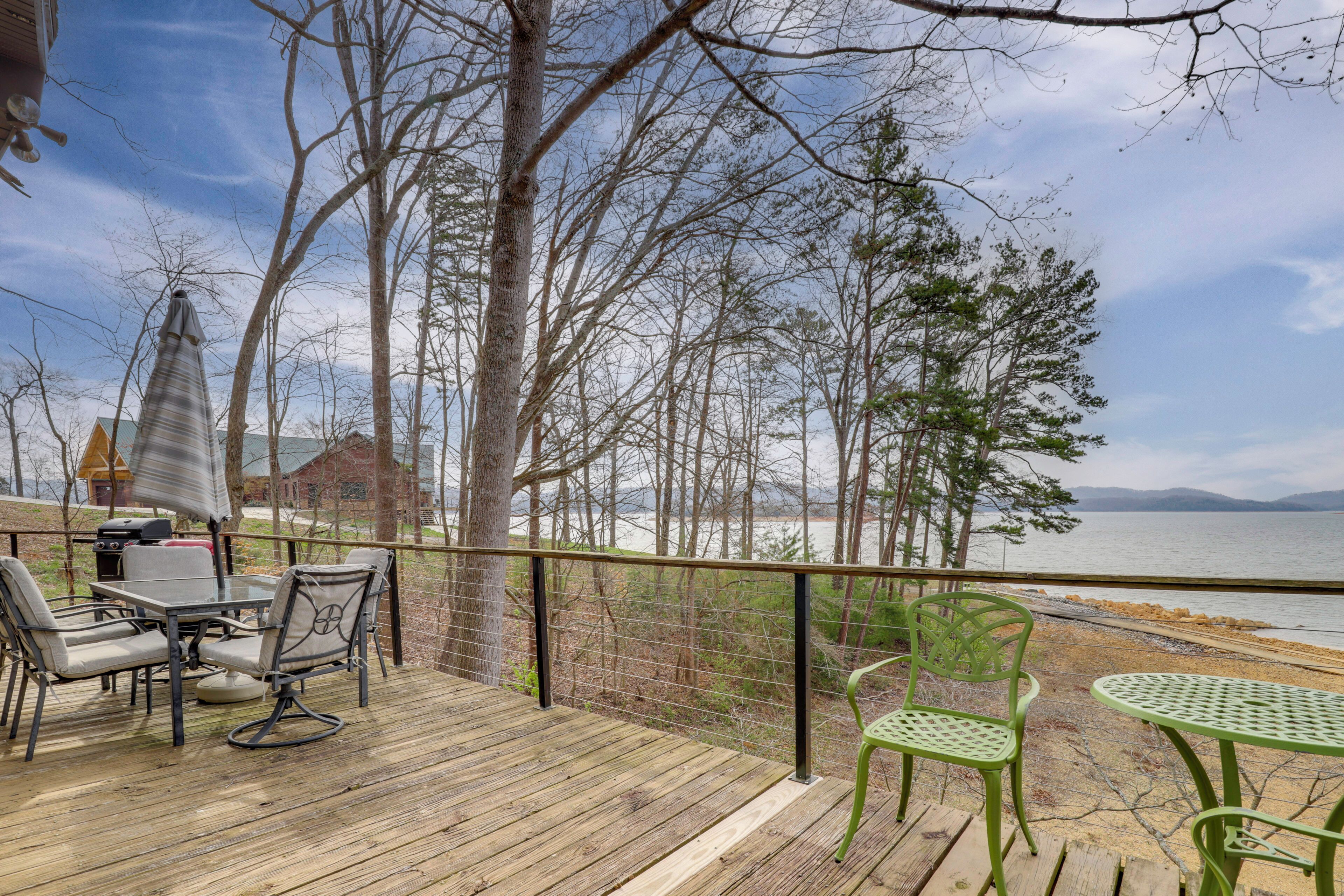 A wooden deck with outdoor furniture, a view of the lake, and a house in the background.