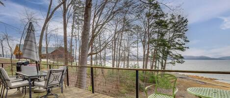 A wooden deck with outdoor furniture, a view of the lake, and a house in the background.