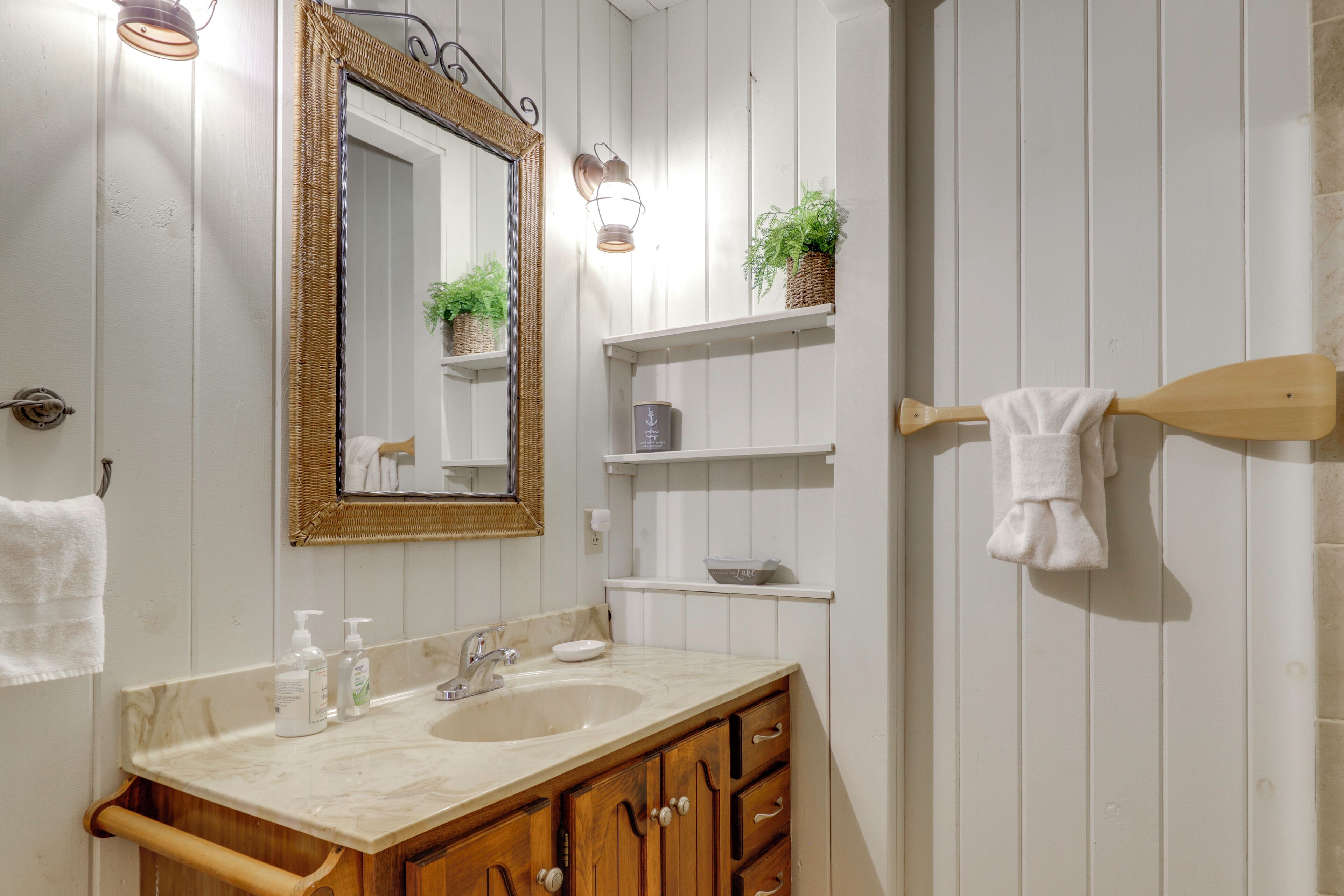 A bathroom with a sink, mirror, towel rack, and shelves with plants.