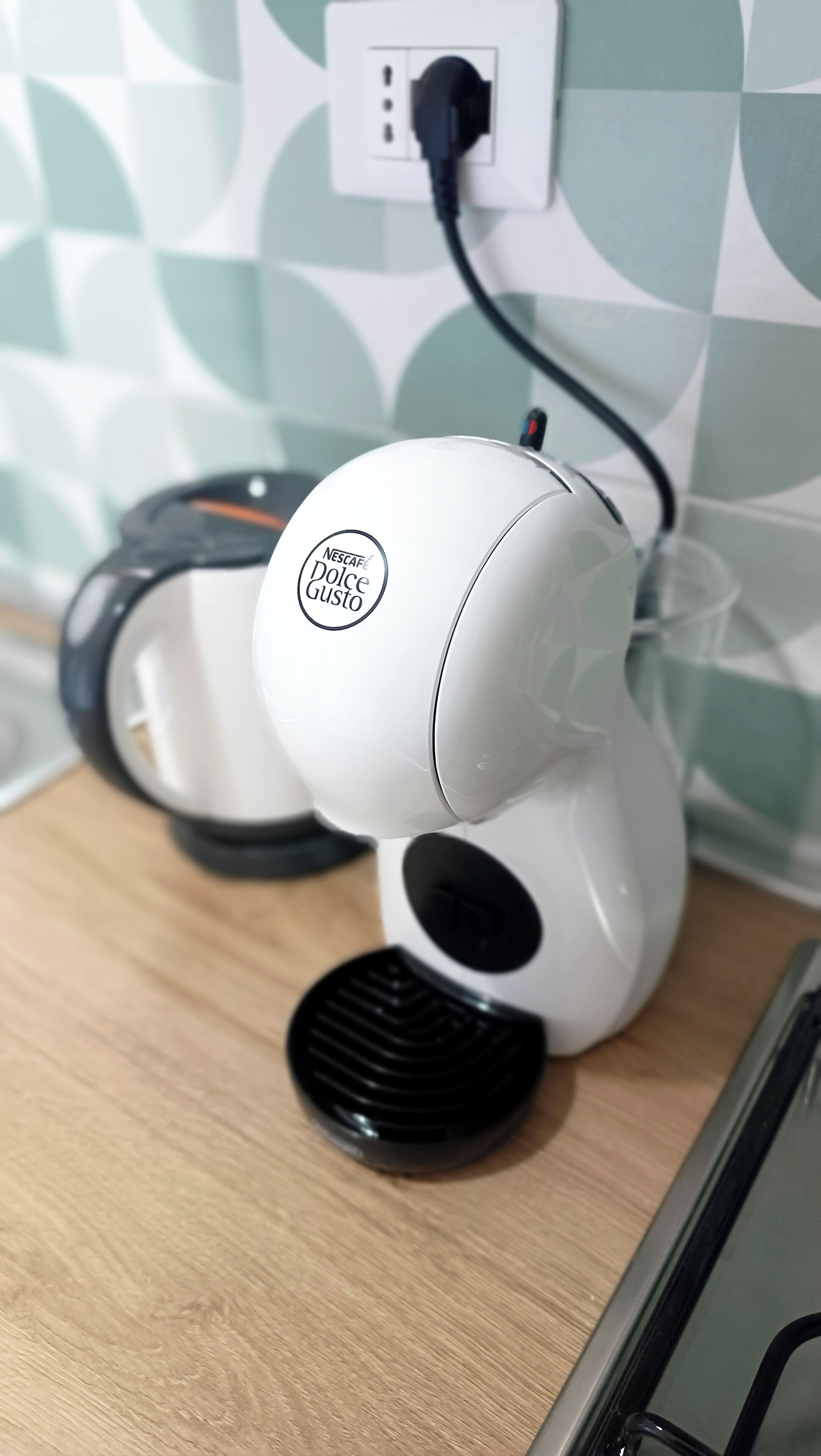 Een Nescafe Dolce Gusto koffiemachine op een houten ondergrond, met een stopcontact op de achtergrond.