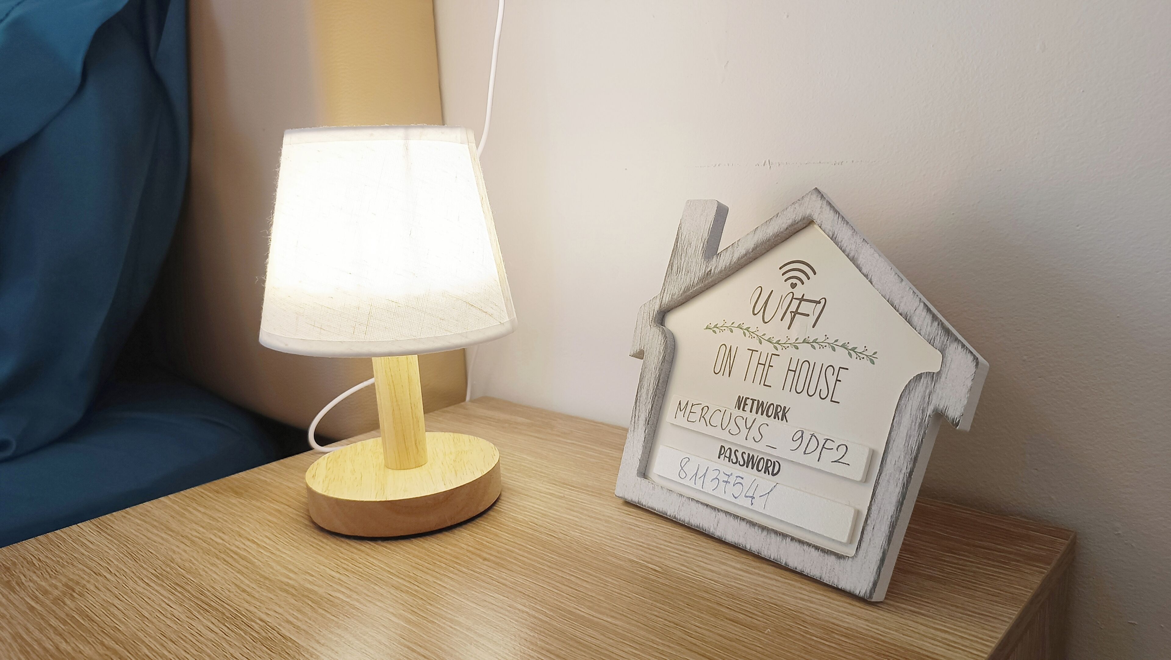A bedside table with a lamp and a framed sign displaying a Wi-Fi password.