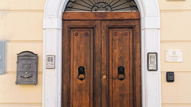 Een dubbele houten deur met een witte boog, een brievenbus en een huisnummerplaatje.