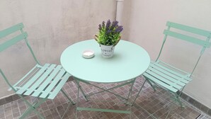 Een kleine ronde tafel met een plant in pot en een kaars, omringd door twee groene stoelen, op een betegeld terras.
