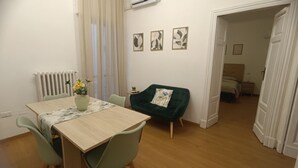 Een eetgedeelte met een tafel, stoelen, een vaas met bloemen, een radiator en een groene fauteuil.