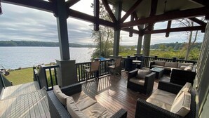 Une terrasse couverte, aménagée avec du mobilier d’extérieur, offrant une vue sur un lac, et un véhicule garé à proximité.