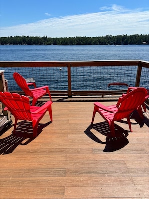 A wooden deck with red chairs facing a body of water and a forested shoreline.