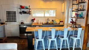 A kitchen with a wooden ceiling, a central island with bar stools, a window above the sink, and a patterned rug on the floor.