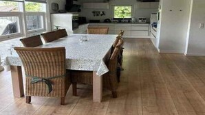 Zona pranzo con tavolo e sedie, cucina sullo sfondo e vista dalla finestra.