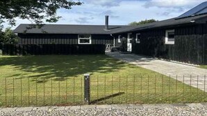Un edificio di due piani con facciata scura, un camino ben visibile e un vialetto lastricato che porta a un ingresso chiuso da cancello.