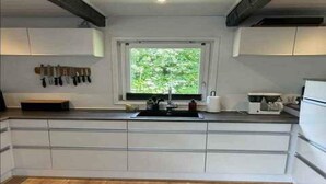 Una cucina con un'ampia finestra, mobili bianchi, pavimento in legno e una macchina per caffè.