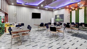 Une salle de conférence dotée de plusieurs tables et de chaises, de ventilateurs de plafond, d’un téléviseur à écran plat et d’un mur vert orné d’un tableau.