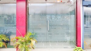 Une entrée d’immeuble avec une porte en verre, des plantes en pot et un mur rouge.