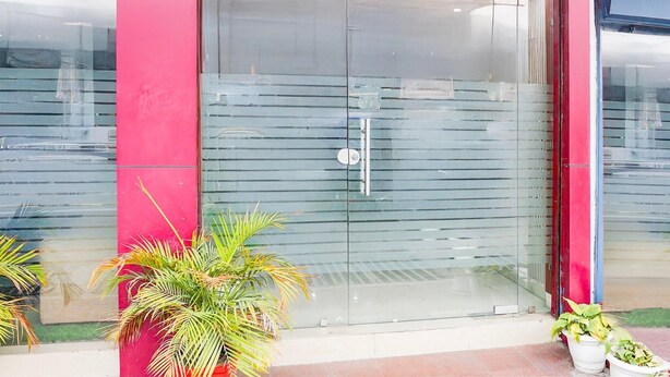 Une entrée d’immeuble avec une porte en verre, un mur rouge et des plantes en pot.