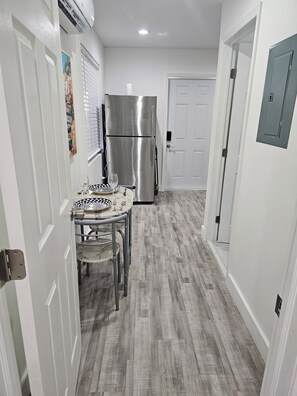 A narrow hallway with a dining table and chairs, a stainless steel refrigerator, and a white door at the end. - Cozy, quiet guest house with AC in vibrant Hollywood. (Hollywood)