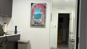 Ett modernt kök med en grå bänkskiva, en papperskorg och en tavla som föreställer ett kustlandskap.