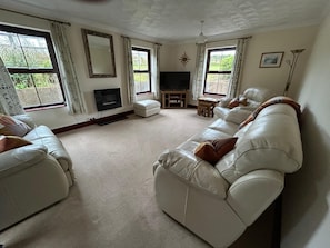 A living room with a sofa, a television, a fireplace, and large windows. - Cosy 3 bedroom cottage in Maidenwells (Pembroke)