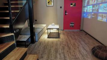 Un interior moderno con una escalera, una puerta roja, una pantalla de proyección y una pequeña mesa con mantel a cuadros.