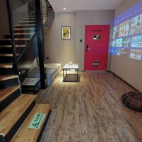 Un interior moderno con una escalera, una puerta roja, una pantalla de proyección y una pequeña mesa con mantel a cuadros.