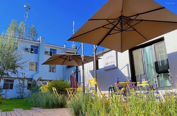 A building with outdoor seating, including yellow chairs and brown umbrellas, and a sign that reads 'FREE TRAVEL WELL BEING.' - Liangzhu Guesthouse (Ürümqi)