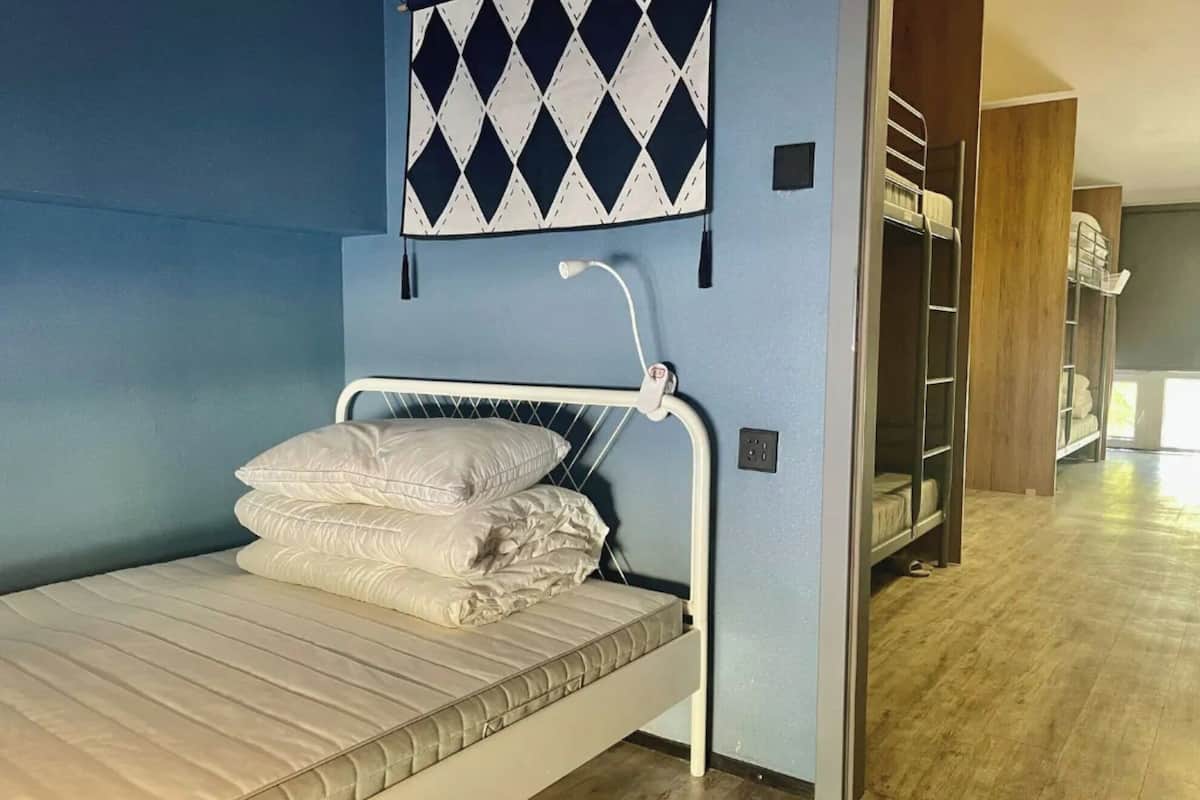 A bunk bed with a mattress and pillows, a wall-mounted light fixture, and a blue wall with a diamond-patterned decoration.
