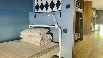 Un lit superposé avec un matelas et des oreillers, un luminaire fixé au mur et un mur bleu orné d’un motif en losanges.