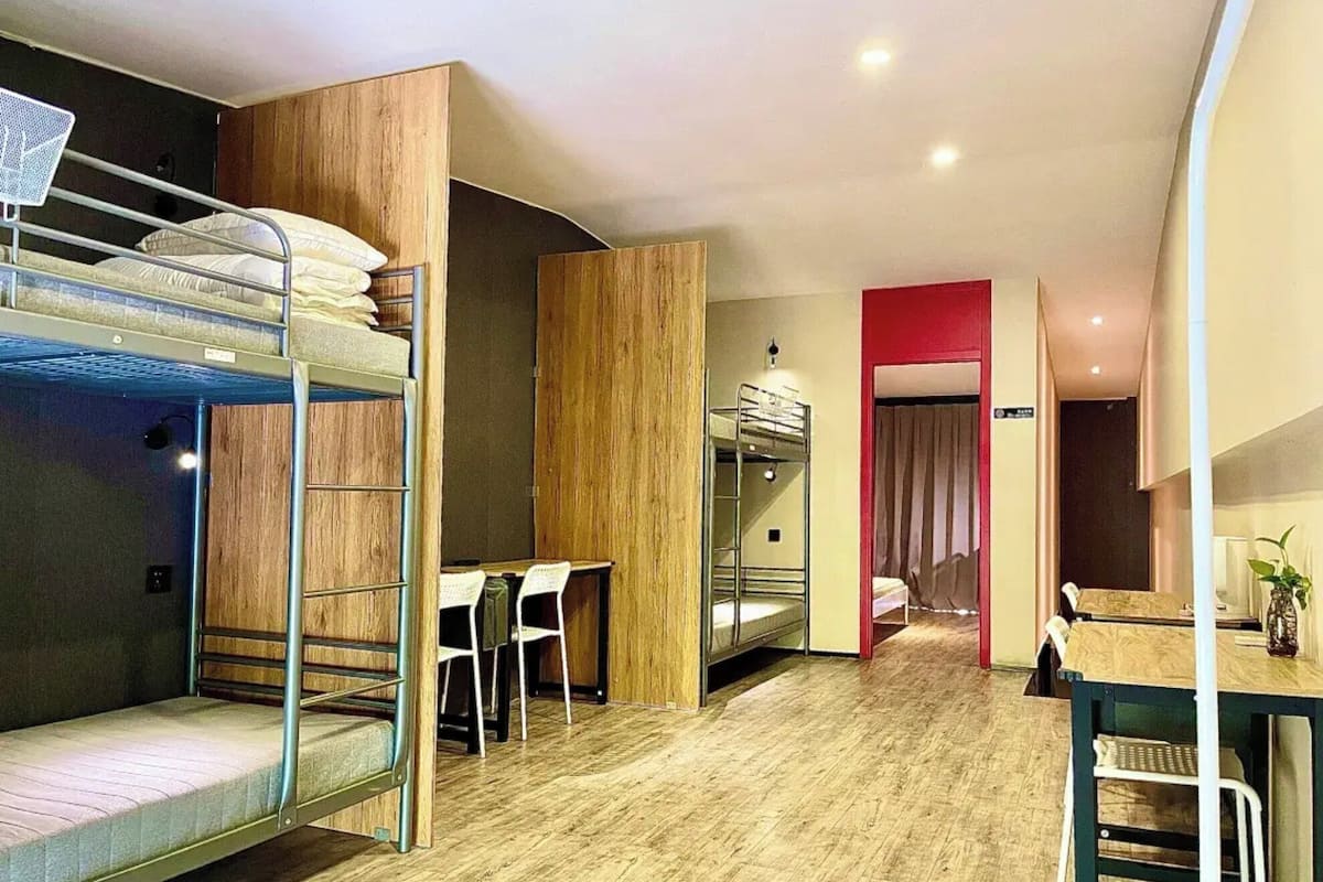 A compact hotel room with bunk beds, a desk, and a dining area.