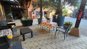 Ein Sitzbereich im Freien mit Korbmöbeln, einem Tisch mit gemustertem Tischläufer, Topfpflanzen und einer Treppe zu einer oberen Ebene.