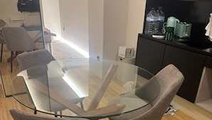 A modern dining area with a glass-top table and grey upholstered chairs. - Downtown River Superior New Flat (Lisbon)