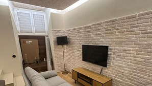 A modern living room with a brick wall, a flat-screen TV, a sofa, a wooden coffee table, and a floor lamp. - Downtown River Superior New Flat (Lisbon)