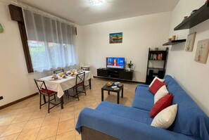 Ein Wohnzimmer mit blauem Sofa, Esstisch und Fernseher.