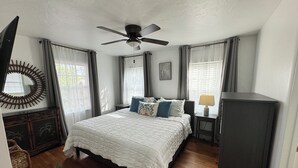 Ein Schlafzimmer mit Bett, Deckenventilator, Nachttisch, Lampe, Spiegel und Kleiderschrank.