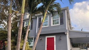 Ein zweigeschossiges Haus mit roter Tür, Hausnummer 9322, umgeben von Palmen und einem kleinen Garten.