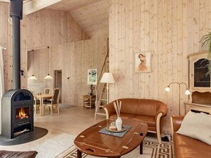 A cozy living room with a fireplace, wooden walls, a leather sofa, and a dining area. - 4 Star Holiday Home in Albaek (Aalbaek)
