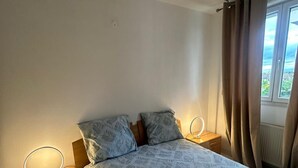 Une chambre à coucher avec un lit, deux tables de chevet avec des lampes, une fenêtre avec des rideaux et une vue sur l’extérieur.