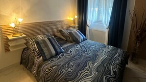 A bedroom with a bed, bedside lamps, a window with curtains, and a radiator. - Beautiful 3-room apartment with unobstructed views, private underground parking, and the Zenith just a stone's throw away (Strasbourg)