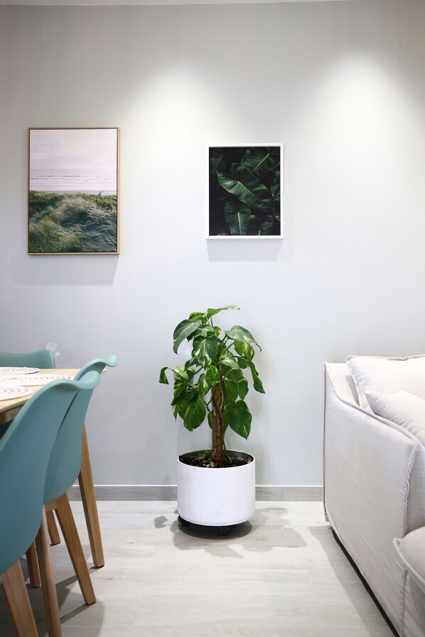 Una habitación con una mesa de comedor, sillas, una planta en maceta, un sofá y dos cuadros en la pared.