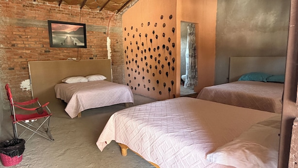 Una habitación con dos camas, una silla plegable roja, una pared de ladrillo y un cuadro en la pared.