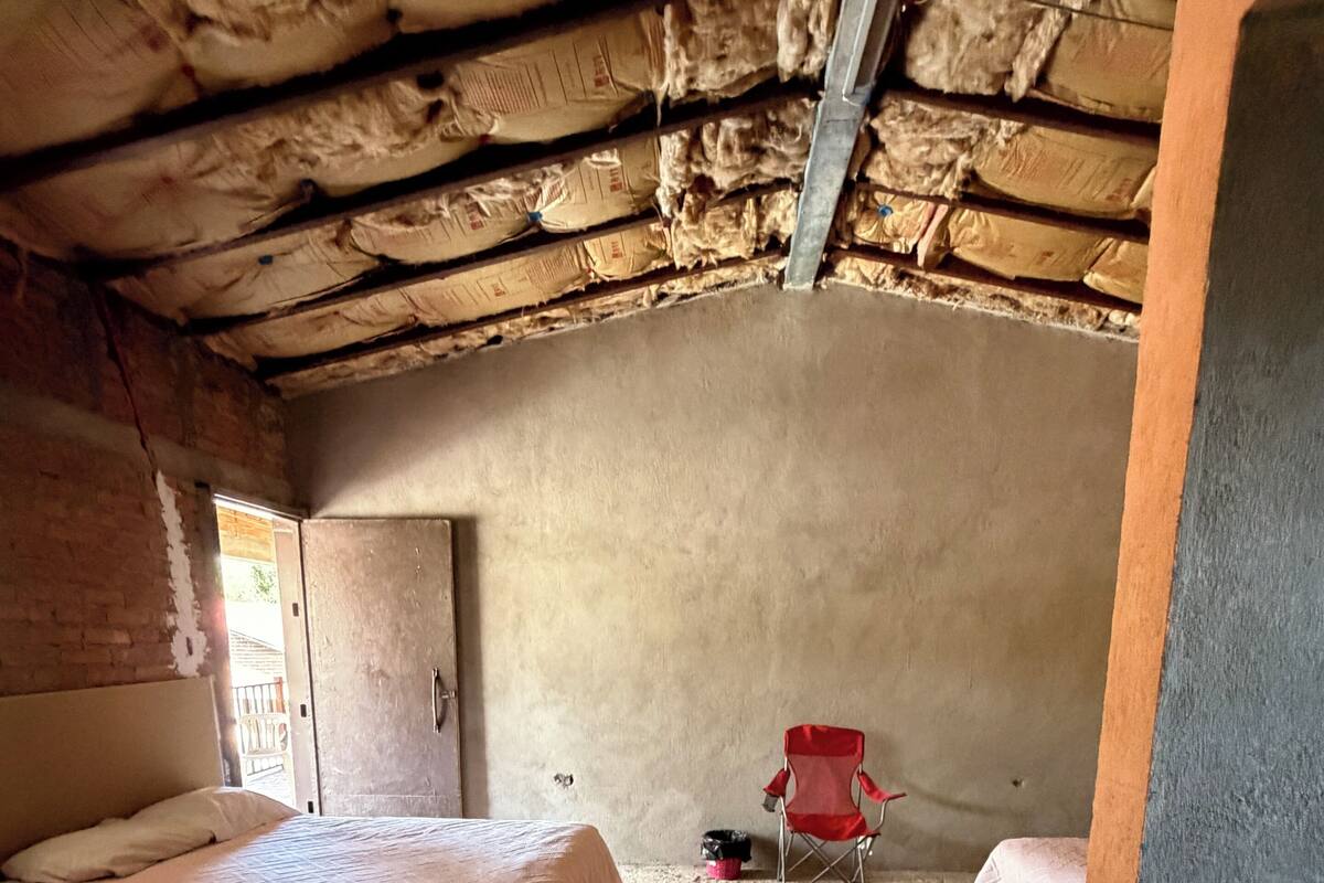 Ein Zimmer mit zwei Betten, einem roten Sessel und einer Betonwand.
